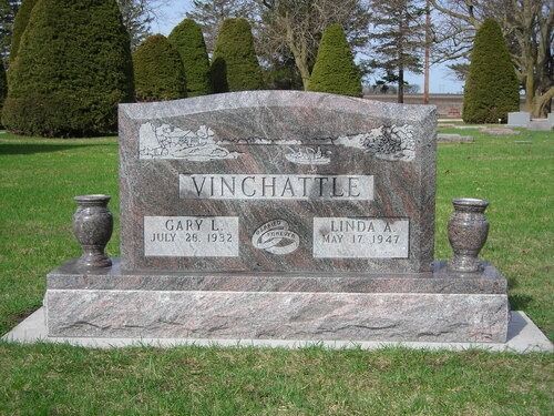 A granite gravestone for Gary and Linda Vinchattle in a grassy cemetery, featuring a central family name and stone vases.