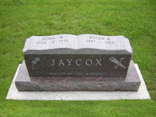 A grey granite gravestone for the Jaycox family, engraved with names and dates, set in a grassy field.