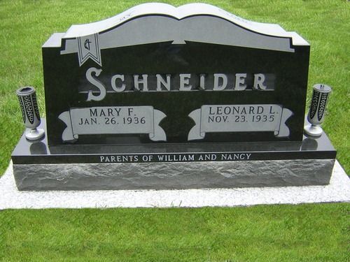 A polished black granite headstone for the Schneider family, with two small vases, set on a grass lawn.