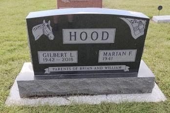 A black granite tombstone for Gilbert and Marian Hood with an engraved horse head, set in a grassy cemetery.