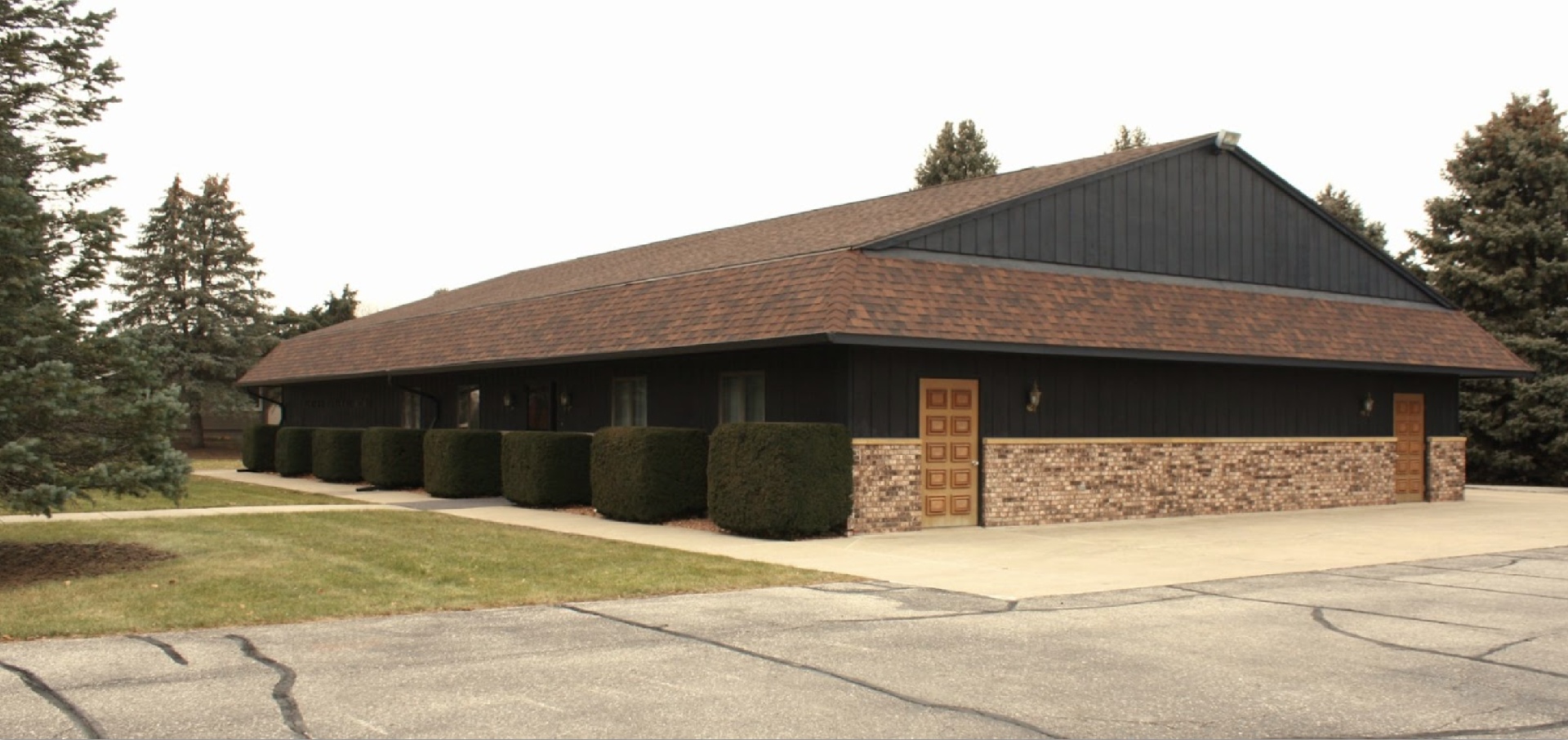 A long, one-story commercial building with dark wood siding, a stone base, a brown roof, and several evenly spaced doors.