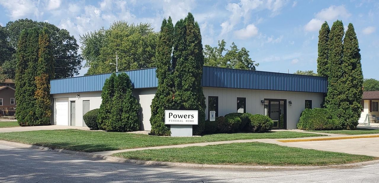 A single-story office building with a blue metal roof, manicured hedges, and a sign reading 