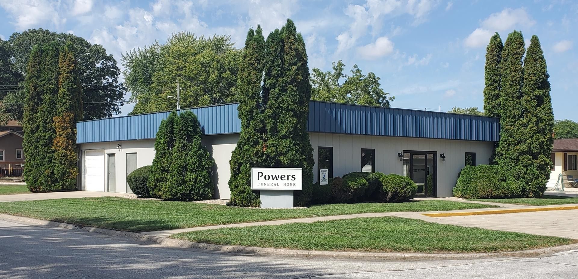A single-story office building with a blue metal roof, manicured hedges, and a sign reading