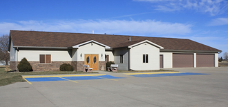 A single-story, light-colored building with a brown roof and stone facade, featuring double doors and a two-car garage.