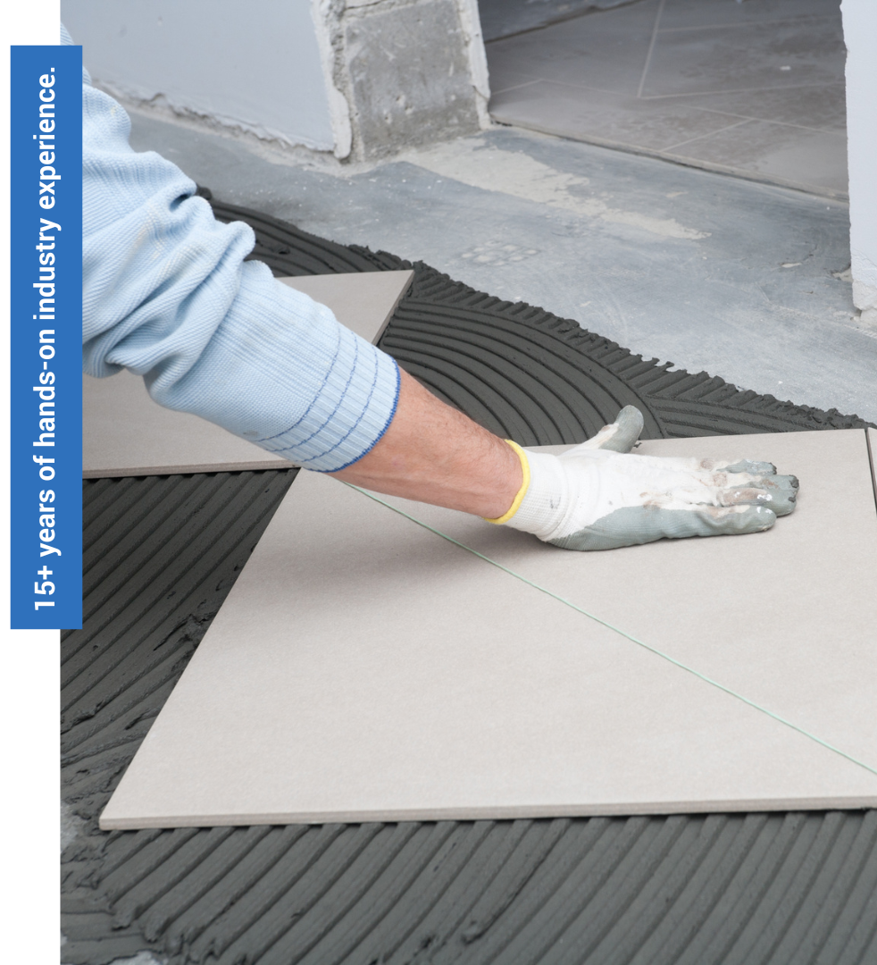 Gloved hand laying a large beige tile on dark adhesive mortar in a construction area