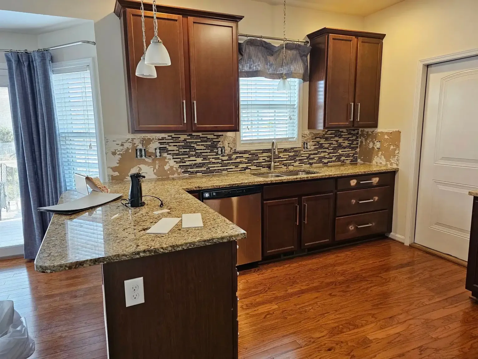 Kitchen with dark wood cabinets, granite counters, mosaic backsplash, and hardwood floors near a sliding glass door.
