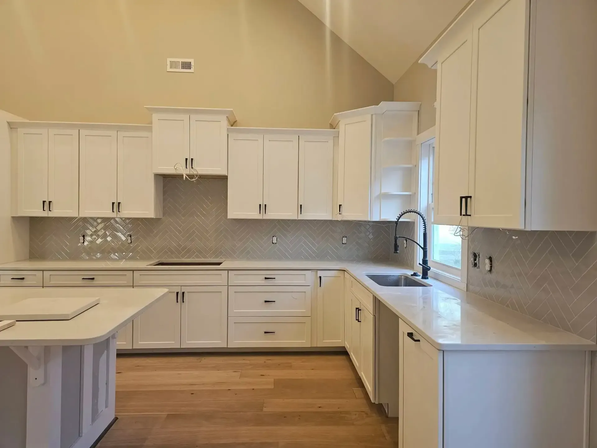 Bright white kitchen with cabinets, marble backsplash, and wood floor; window over the sink.