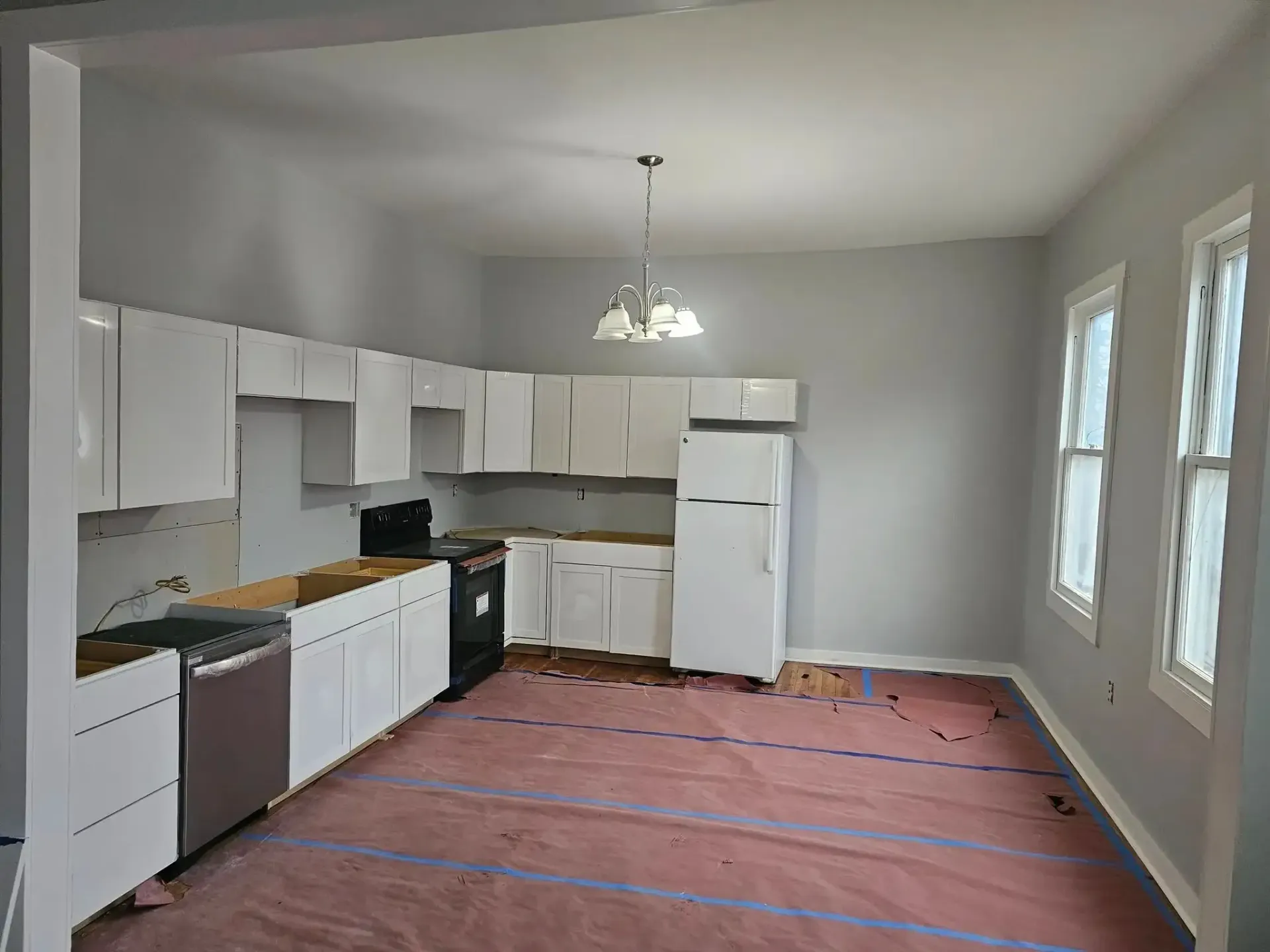 Empty kitchen under renovation with white cabinets, black countertops, and pink floor covering