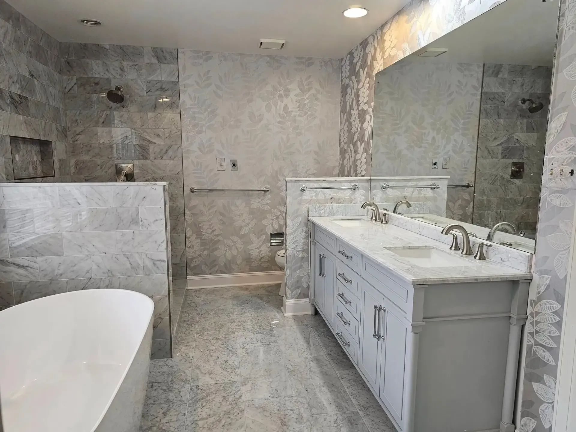 Modern bathroom with gray tile, white vanity, large mirror, and freestanding tub