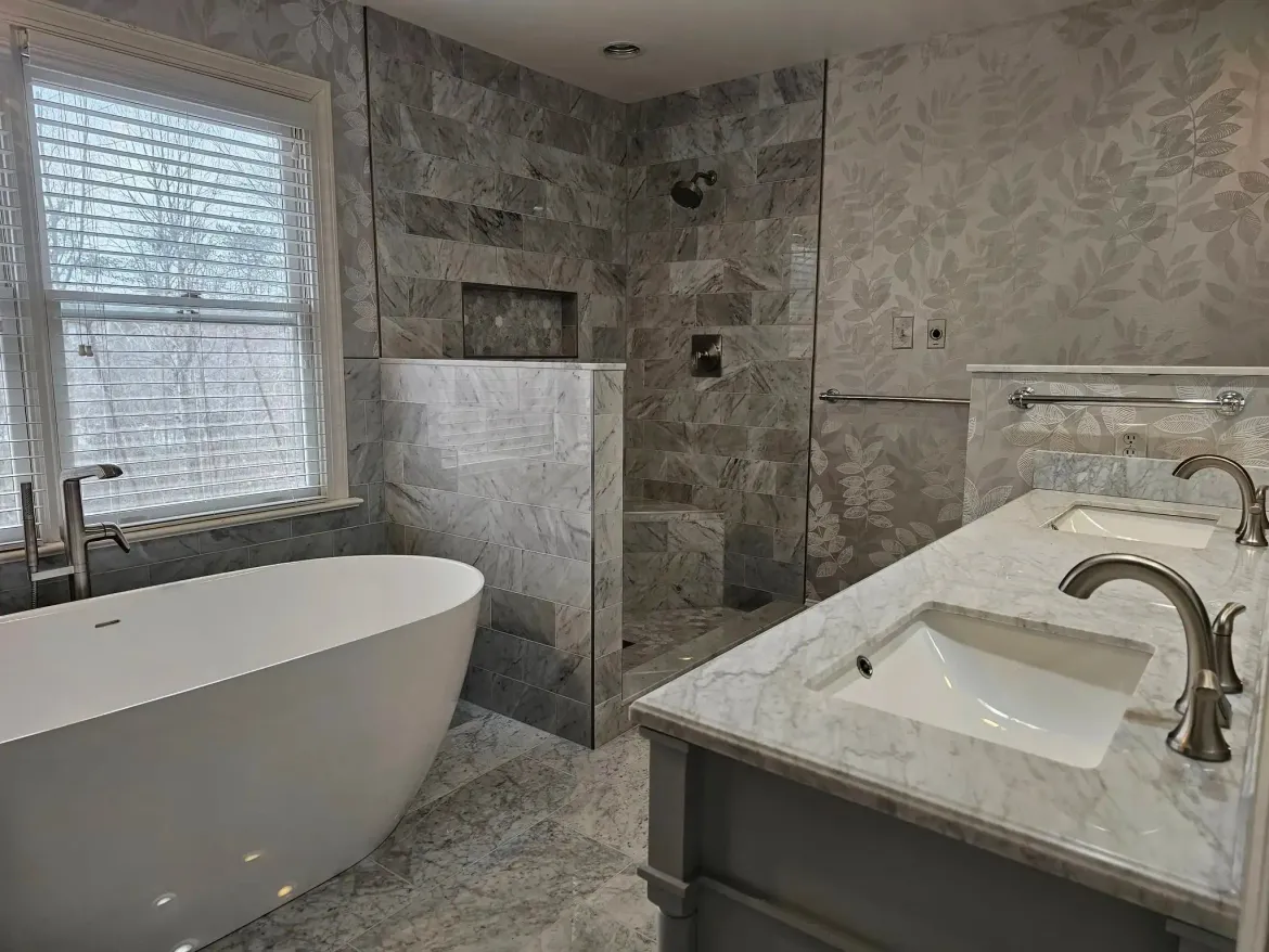 Modern gray-tiled bathroom with freestanding tub, glass shower, and marble double sink vanity