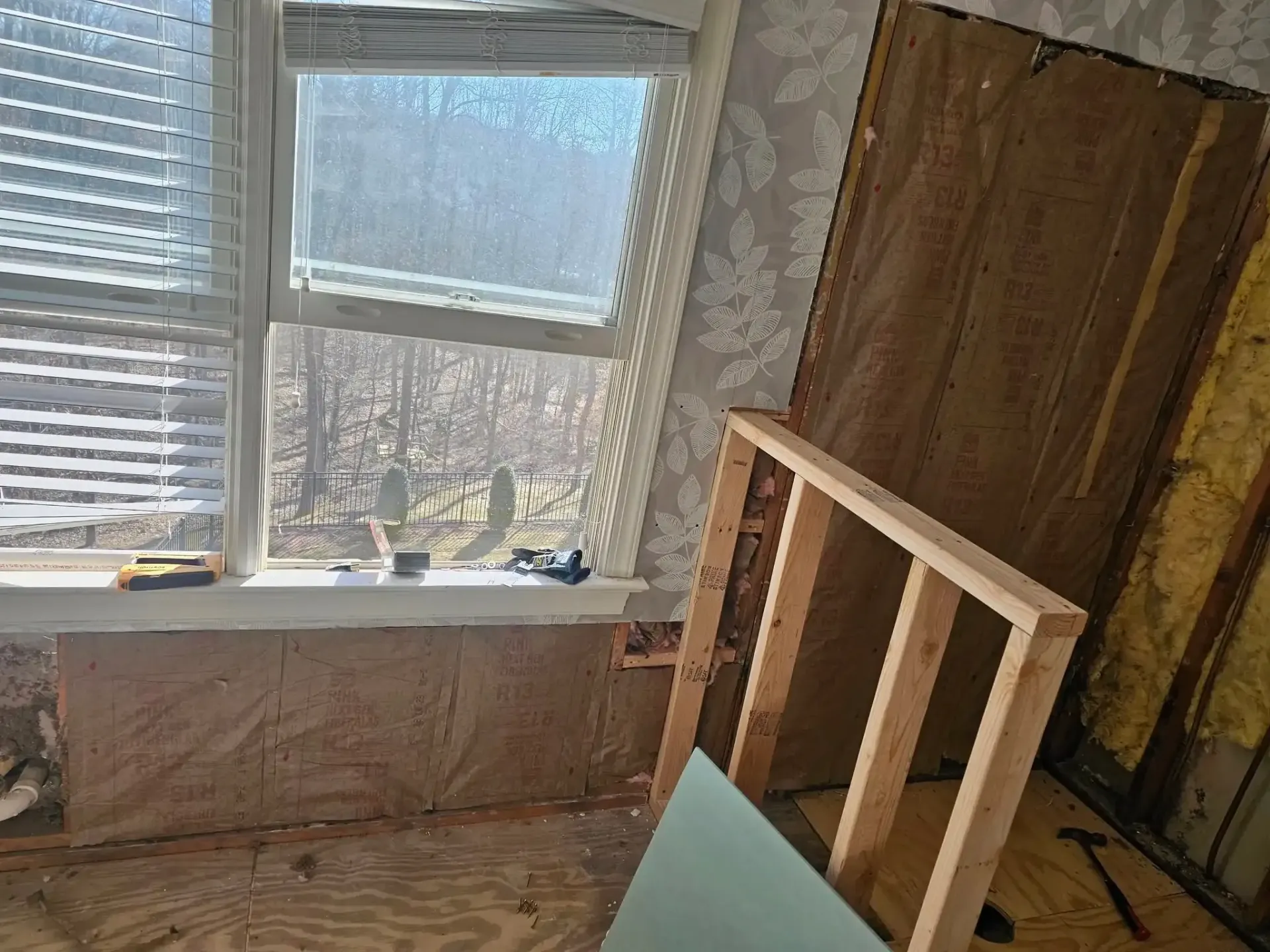 Partially finished room with exposed insulation, window light, and a wooden frame leaning against the wall