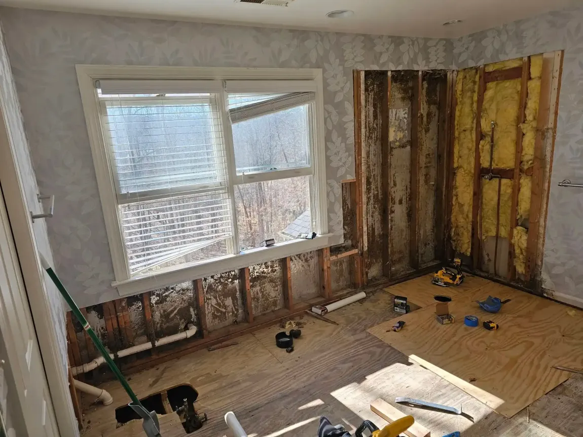 Partially demolished room with exposed wall studs, a window, and construction tools on the floor.
