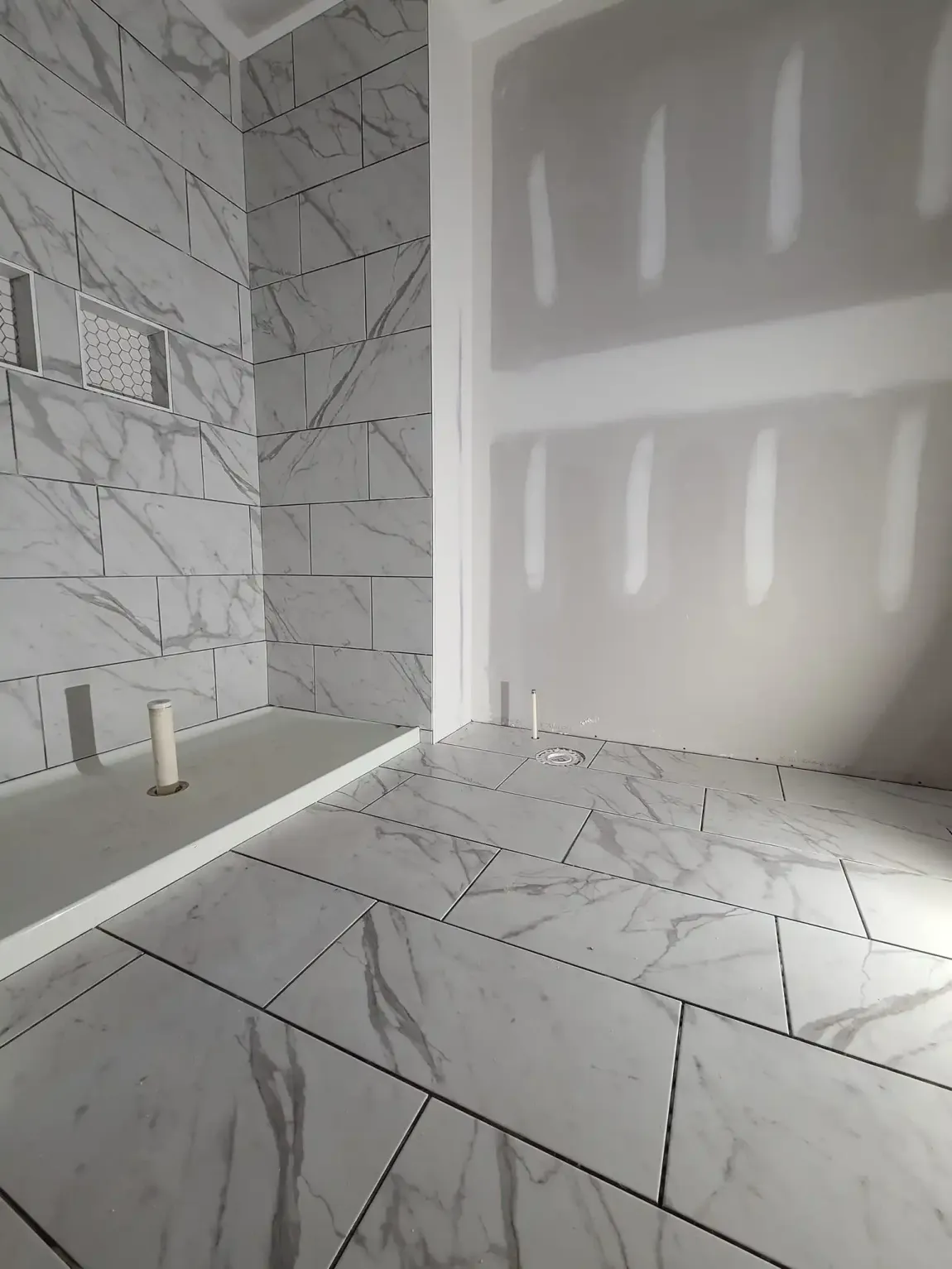 Tiled bathroom with bathtub and shower walls, lit by daylight through a window.
