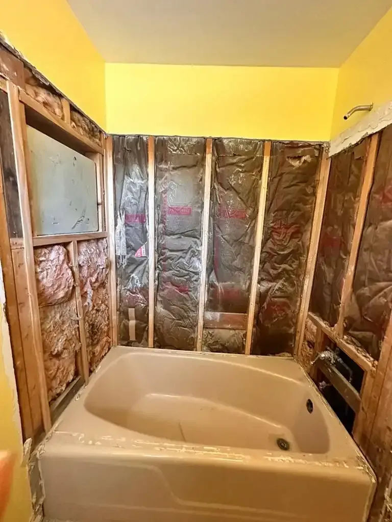 Bathroom under renovation with a bathtub, exposed wall insulation, and yellow walls.