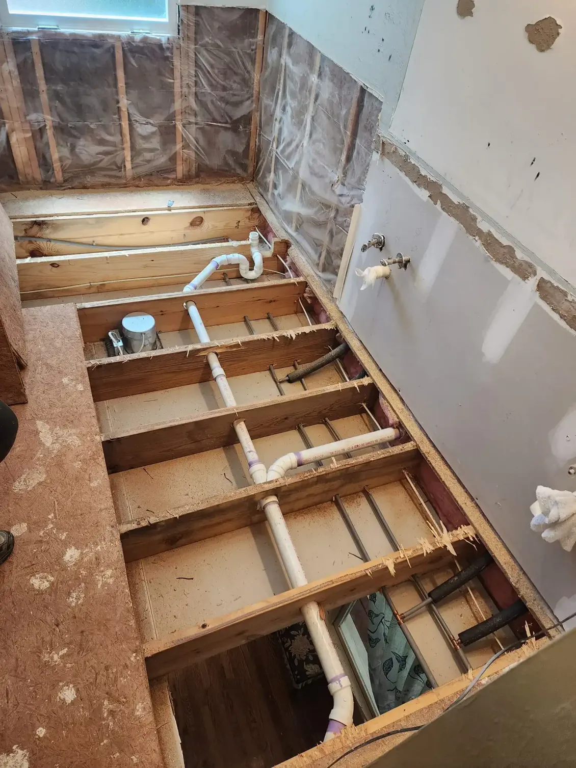 Bathroom floor stripped to joists during renovation, with exposed plumbing and damaged walls.