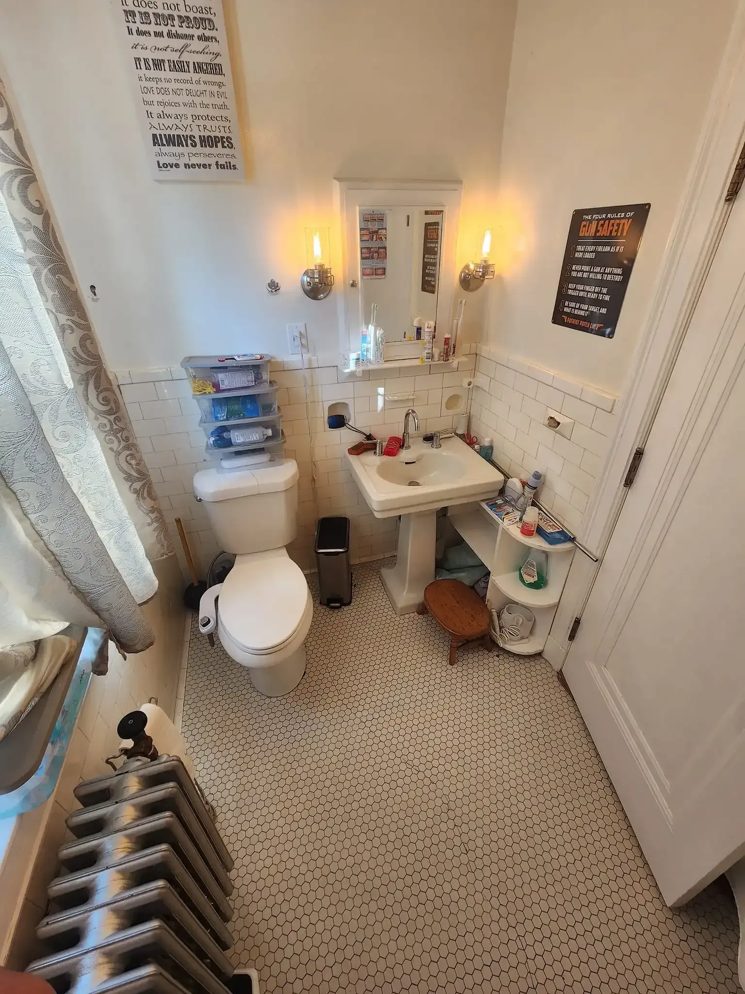 Small, bright bathroom with toilet, sink, mirror lights, patterned floor, and window curtains