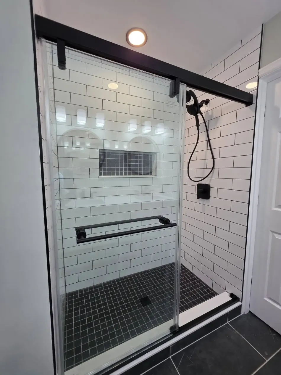 Modern glass shower enclosure with black fixtures and white tiled walls in a bathroom