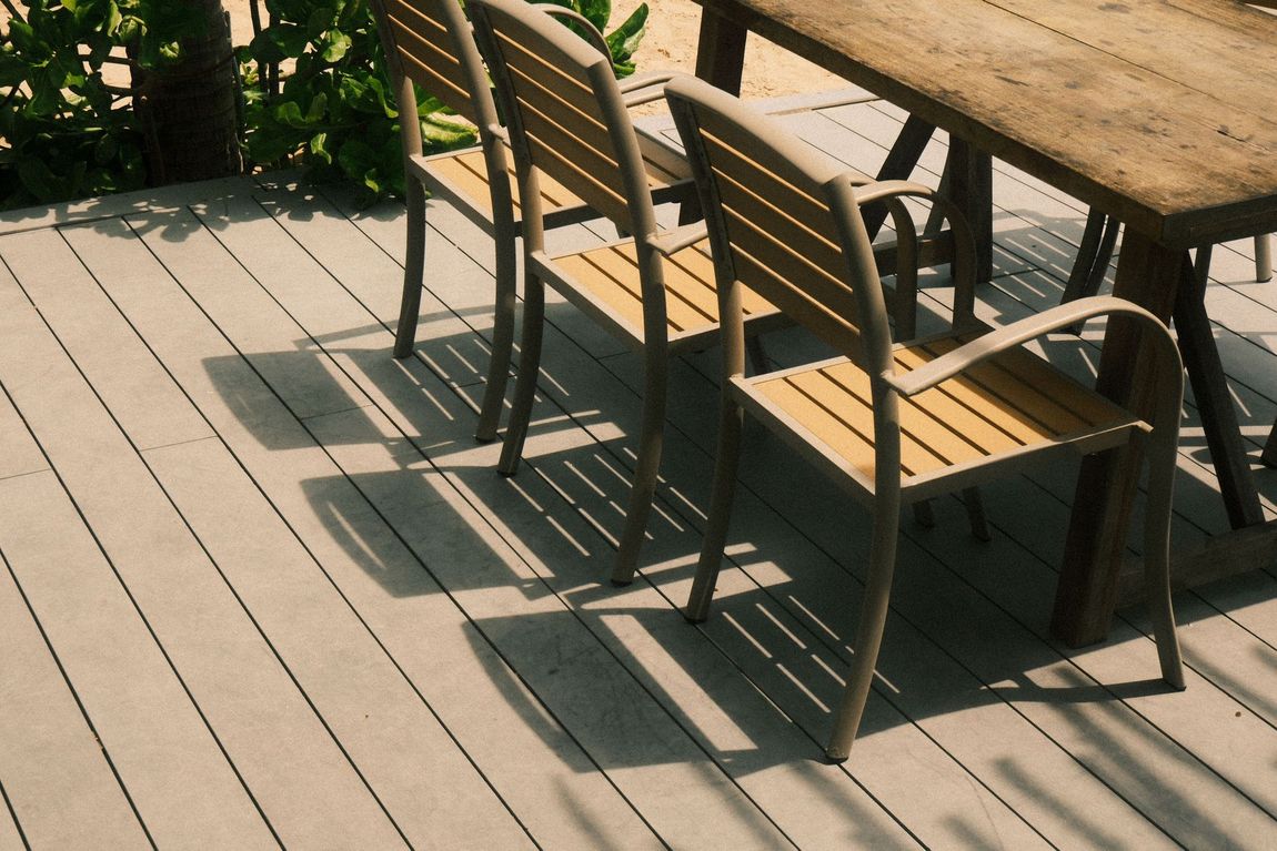 Wooden patio table and chairs casting shadows on a sunlit deck