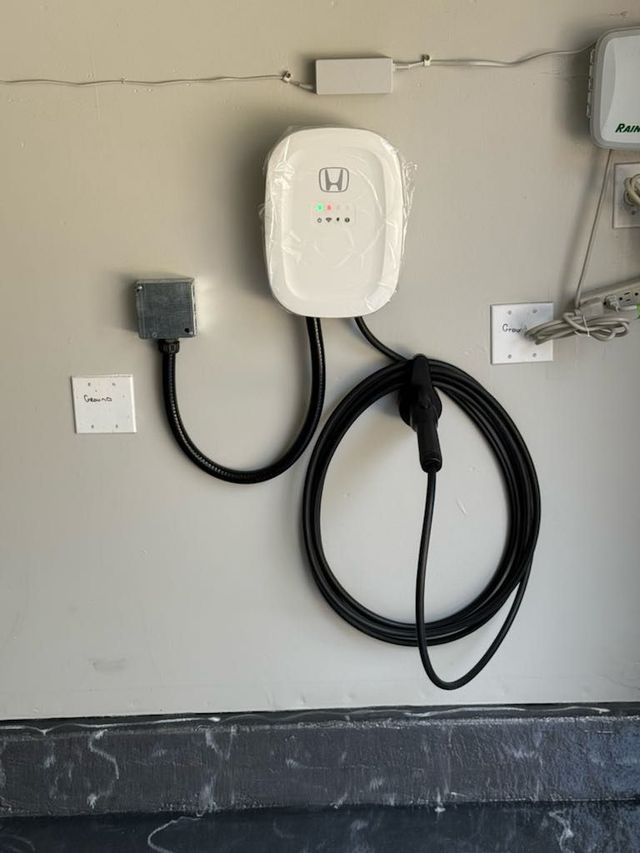 White EV charger mounted on a gray wall, with a black cable and connector.