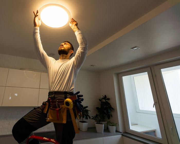 Electrician on a ladder installing a ceiling light fixture in a home.