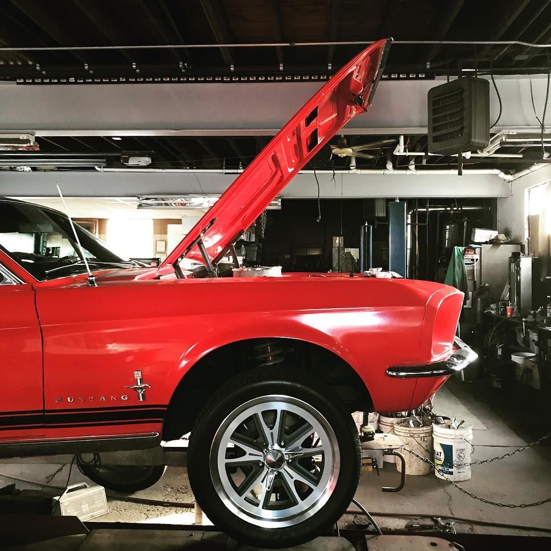 Red classic Mustang car with hood open in a garage, being worked on.