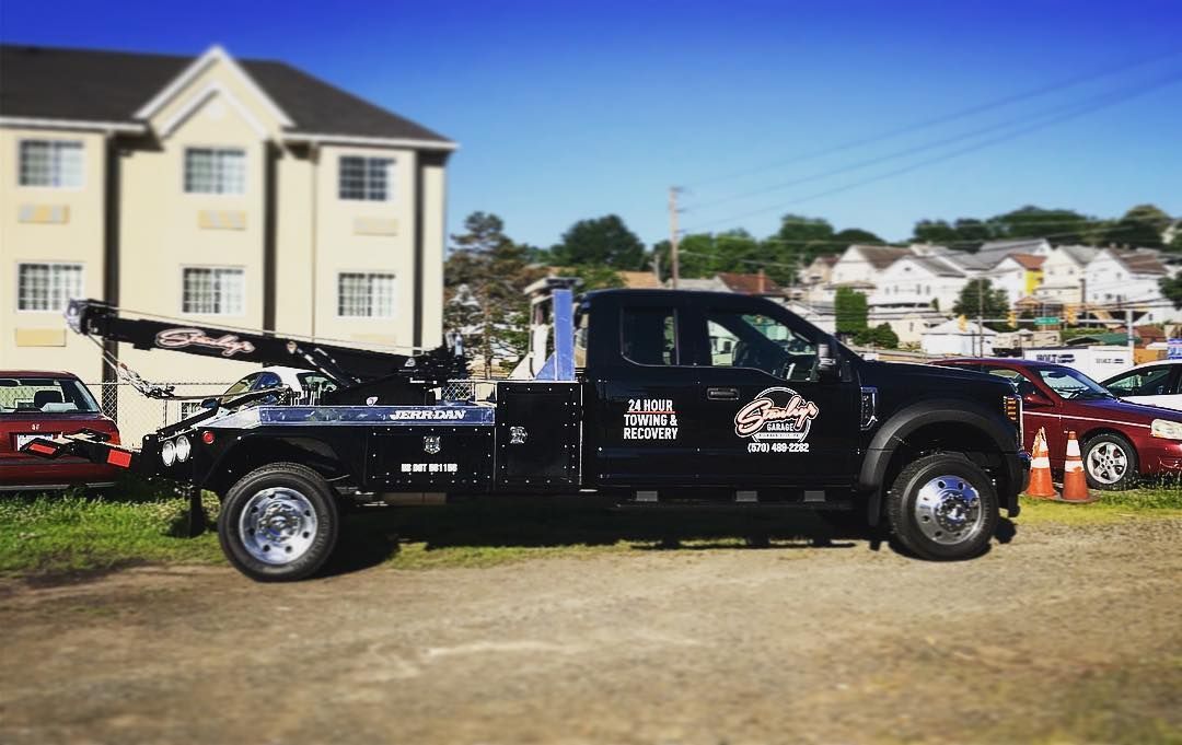 Black tow truck parked in front of a building on a sunny day.
