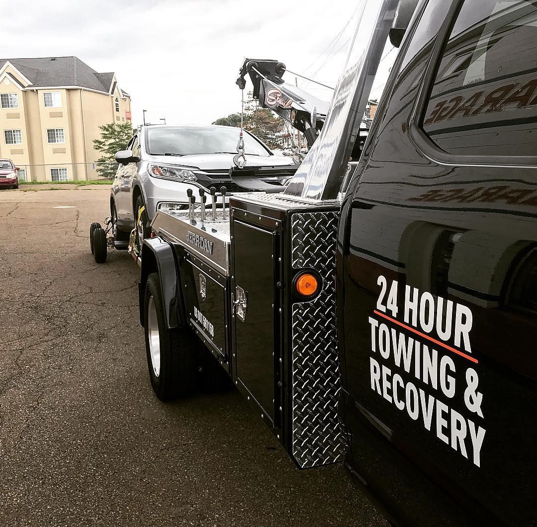 Tow truck towing a silver car in front of a building. 
