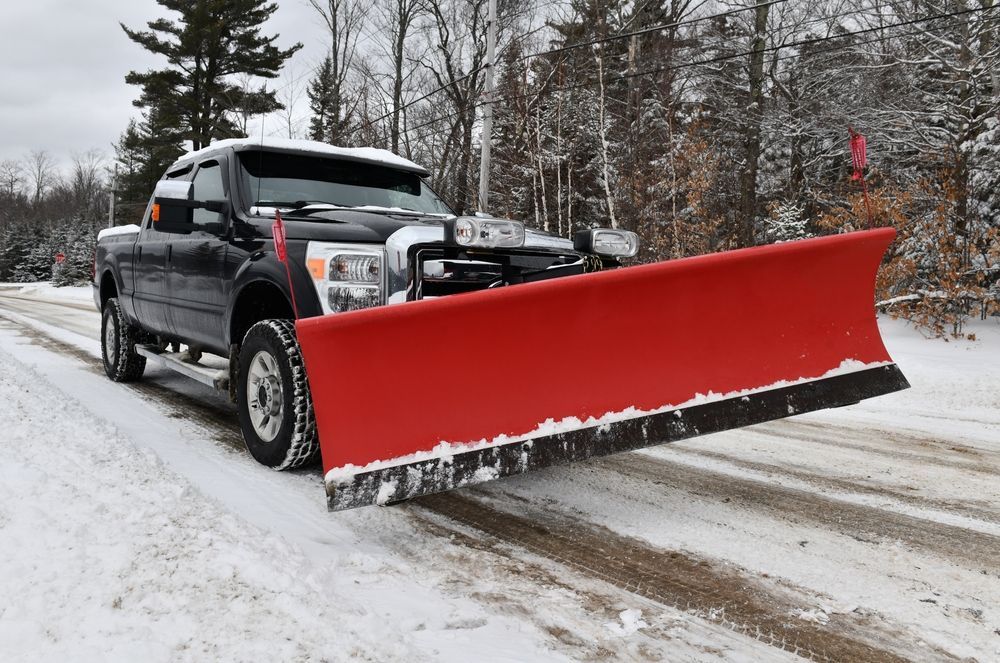 Black pickup truck with a red snowplow clearing a snow-covered road.