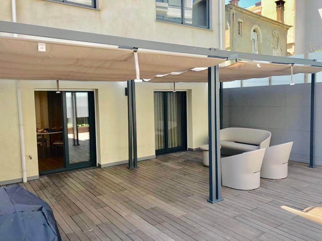 Um deck de madeira com um sofá e cadeiras sob um dossel.