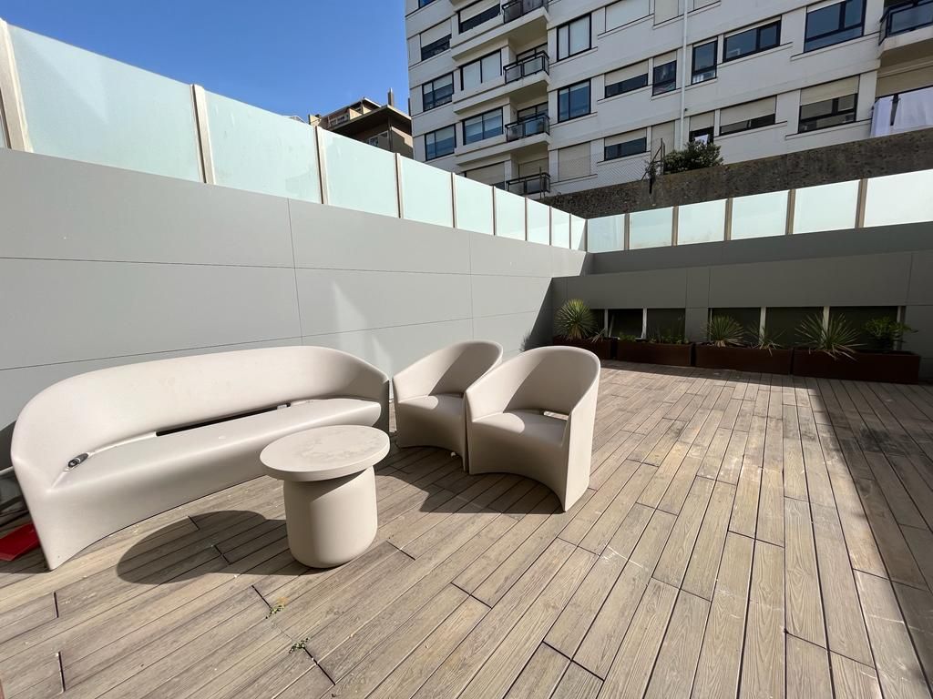 Um pátio com um sofá, cadeiras e uma mesa em frente a um prédio.