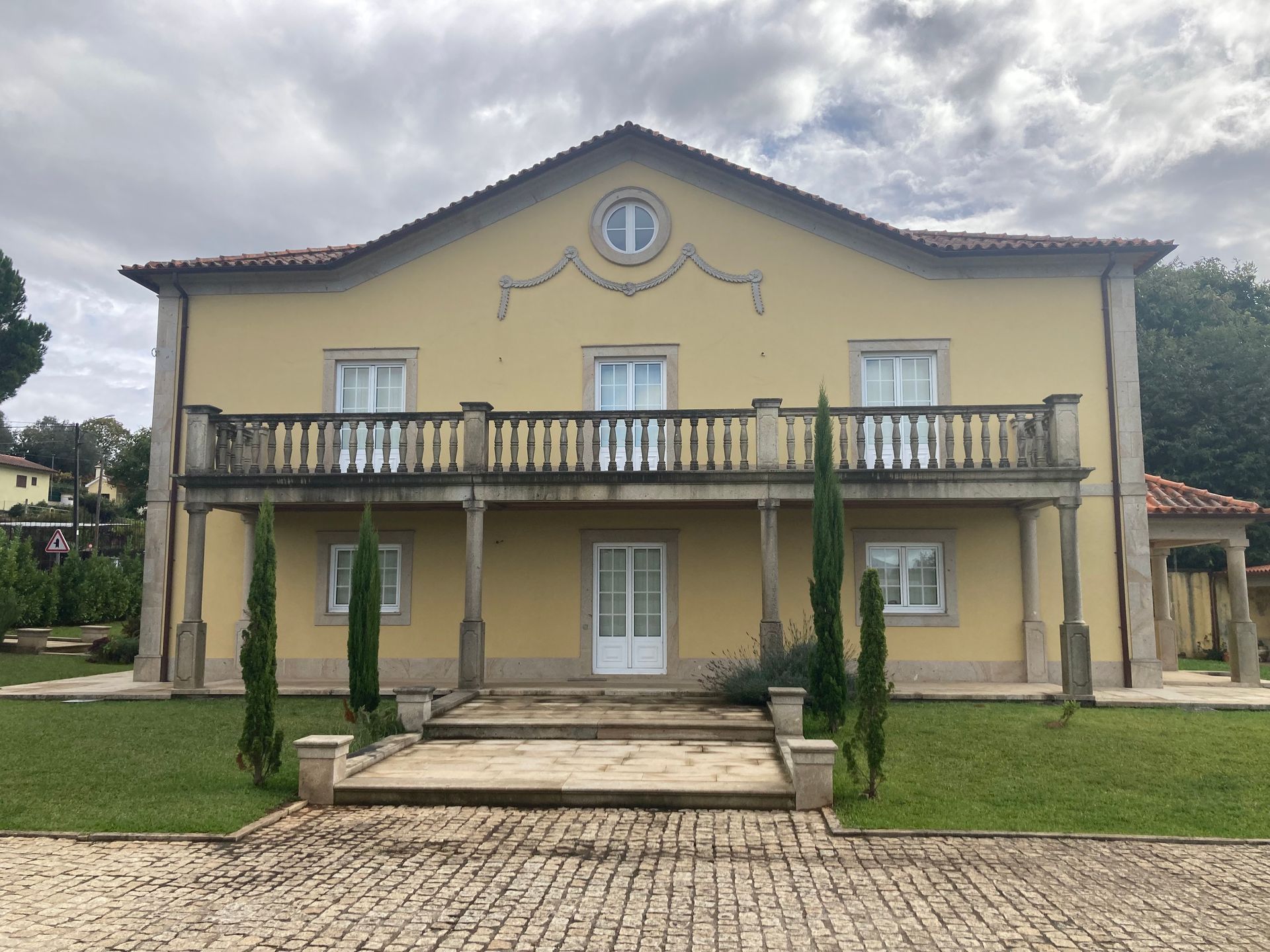 Uma grande casa amarela com uma varanda e uma entrada de tijolos