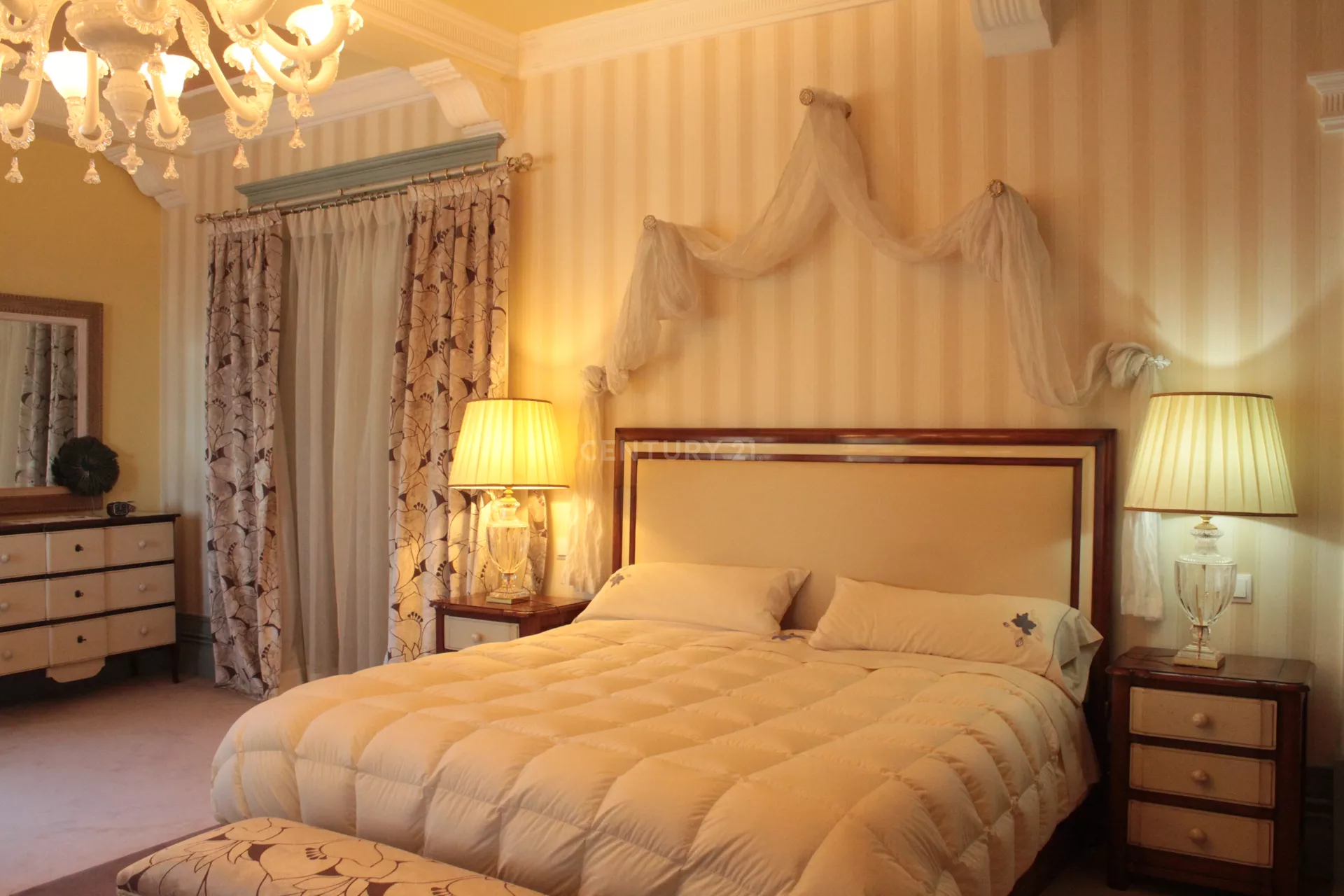 Um quarto com cama, cômoda, mesa de cabeceira, espelho e lustre.