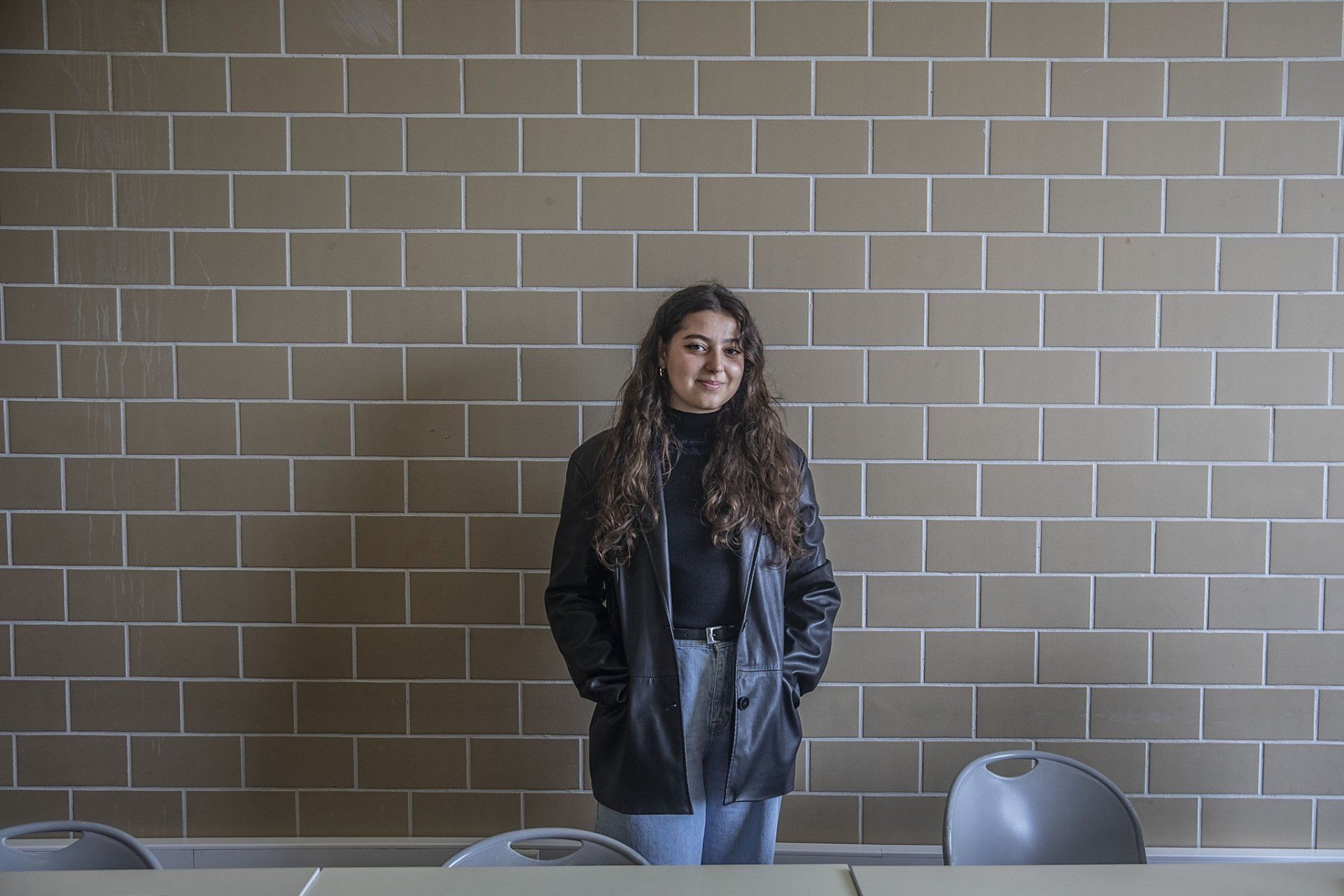 Uma mulher está parada em frente a uma parede de tijolos em uma sala de aula.