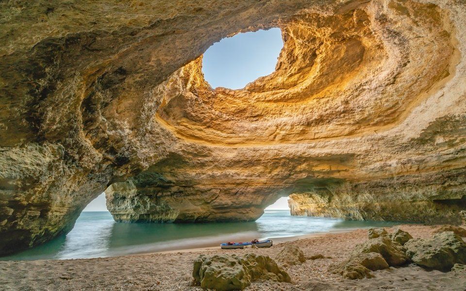 Uma caverna com um buraco no meio que leva a uma praia.