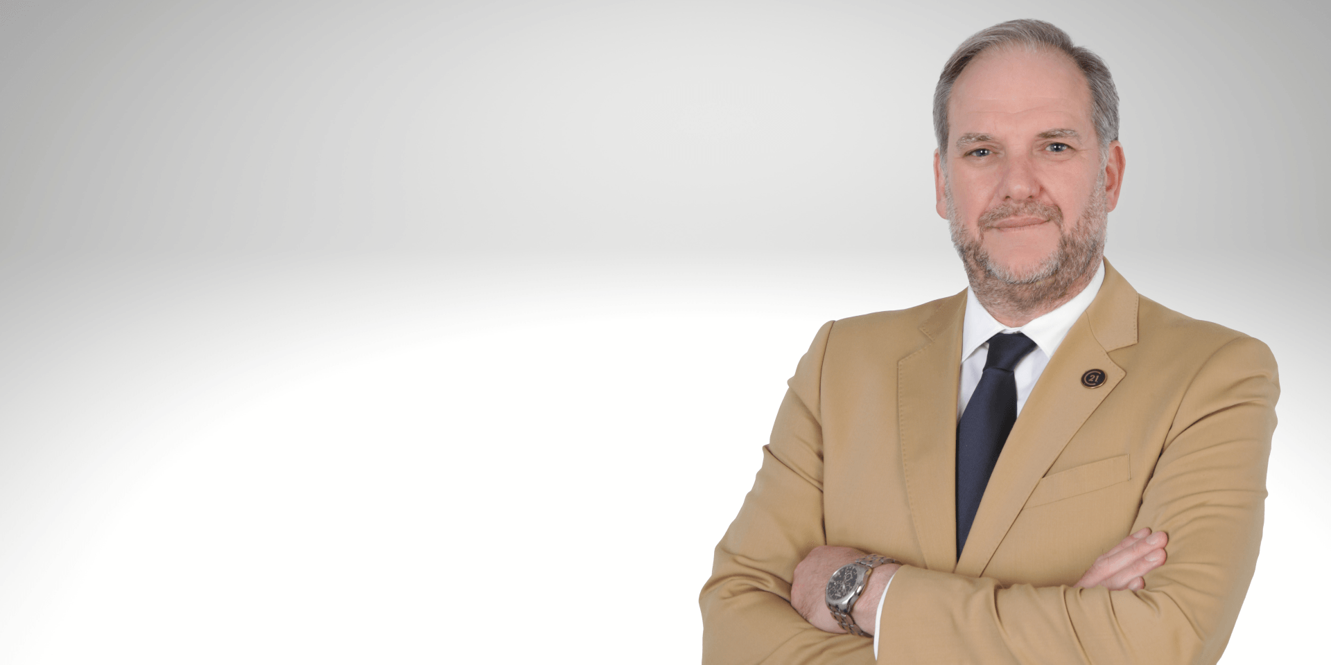 Um homem de terno e gravata está de pé com os braços cruzados.