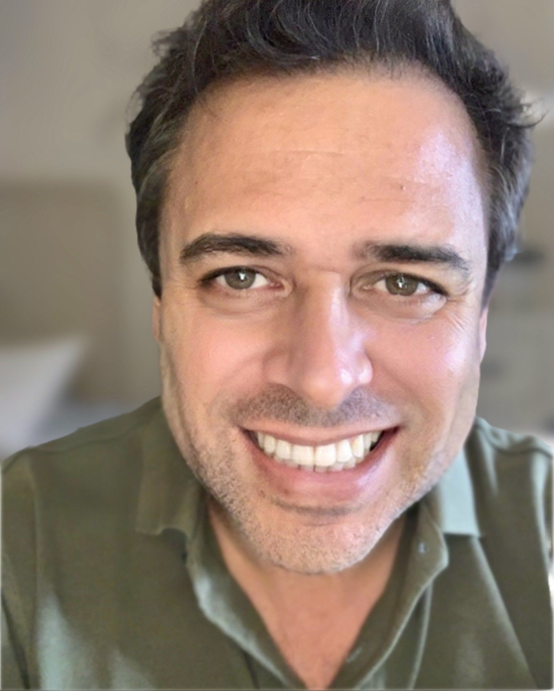 Um homem de camisa verde está sorrindo para a câmera.
