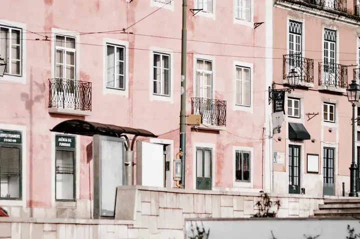 Um prédio rosa com um ponto de ônibus na frente.