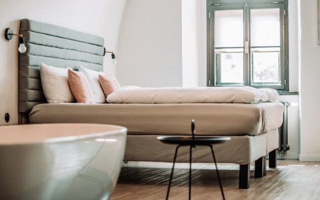 Um quarto de hotel com uma cama, banheira, mesa e janela.