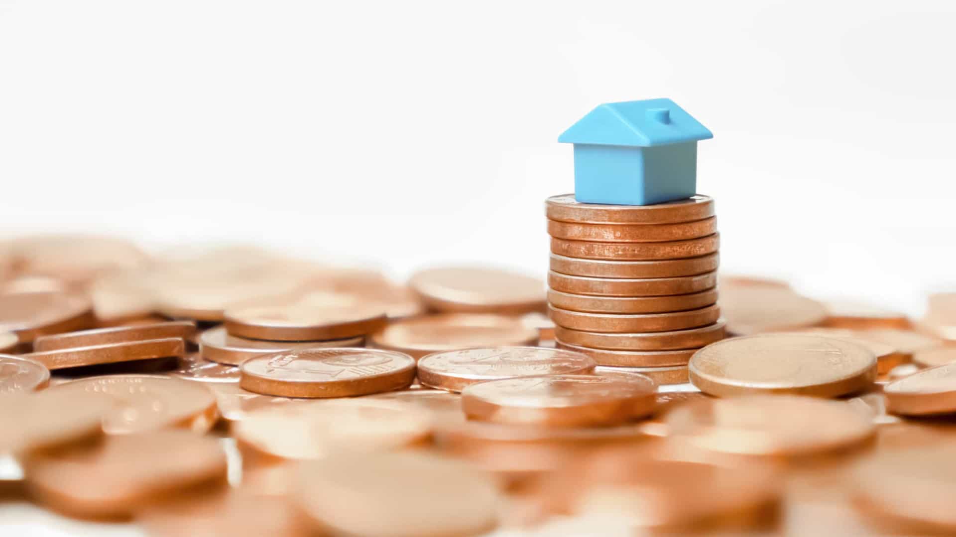 Uma pequena casa está em cima de uma pilha de moedas.