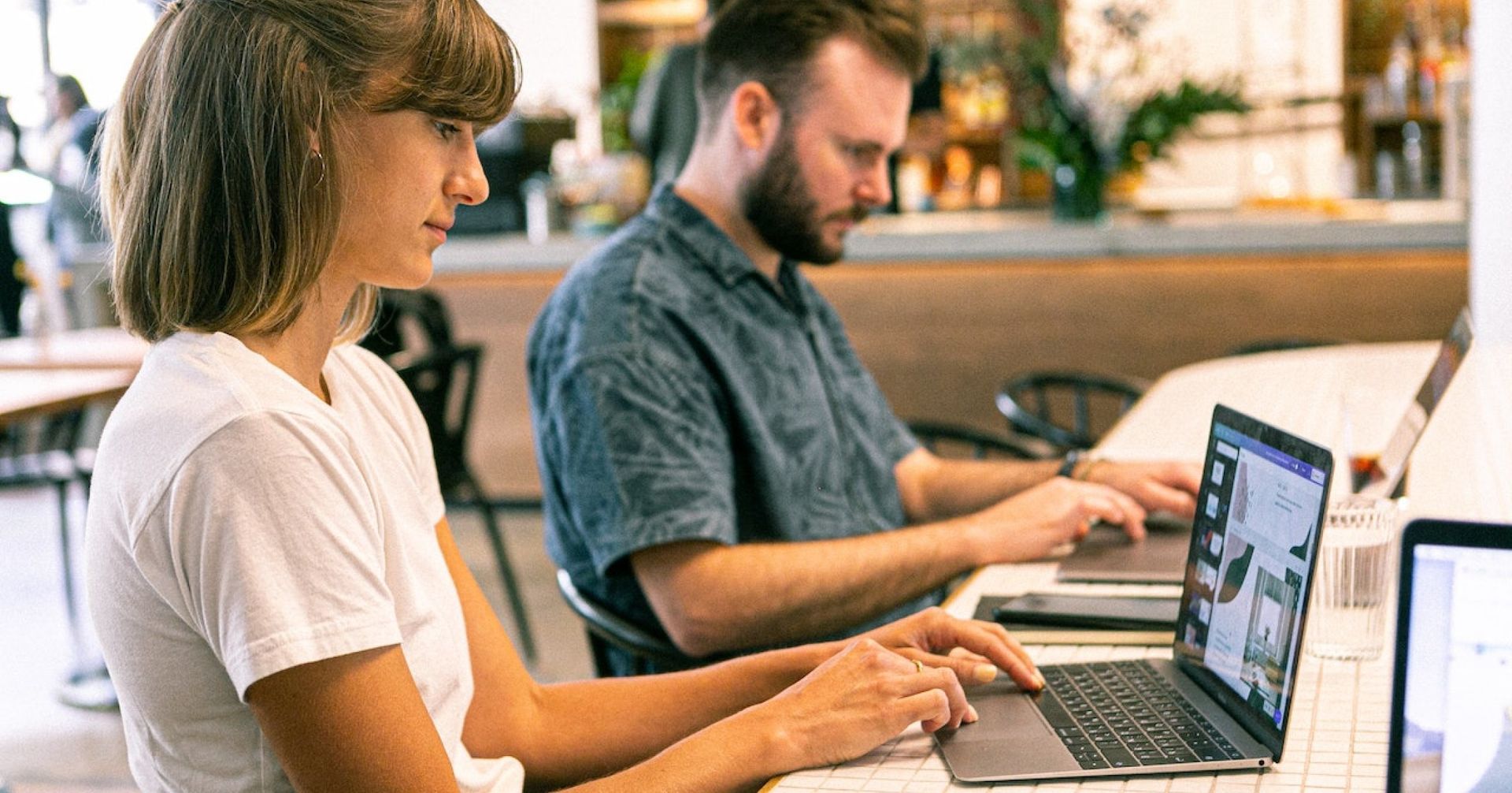Um homem e uma mulher estão sentados à mesa usando laptops.