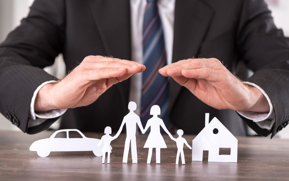 Um homem de terno e gravata está cobrindo um recorte de papel de uma família, um carro e uma casa.