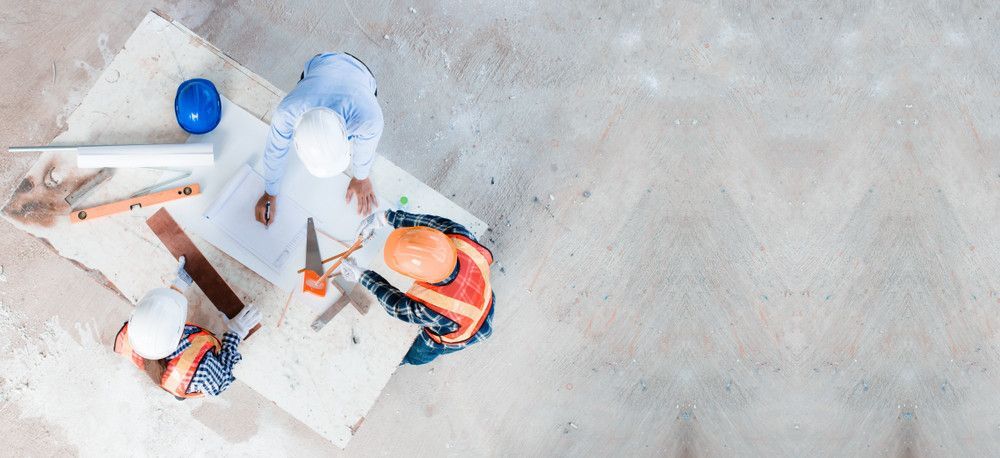Um grupo de trabalhadores da construção civil está sentado à mesa olhando para uma planta baixa.