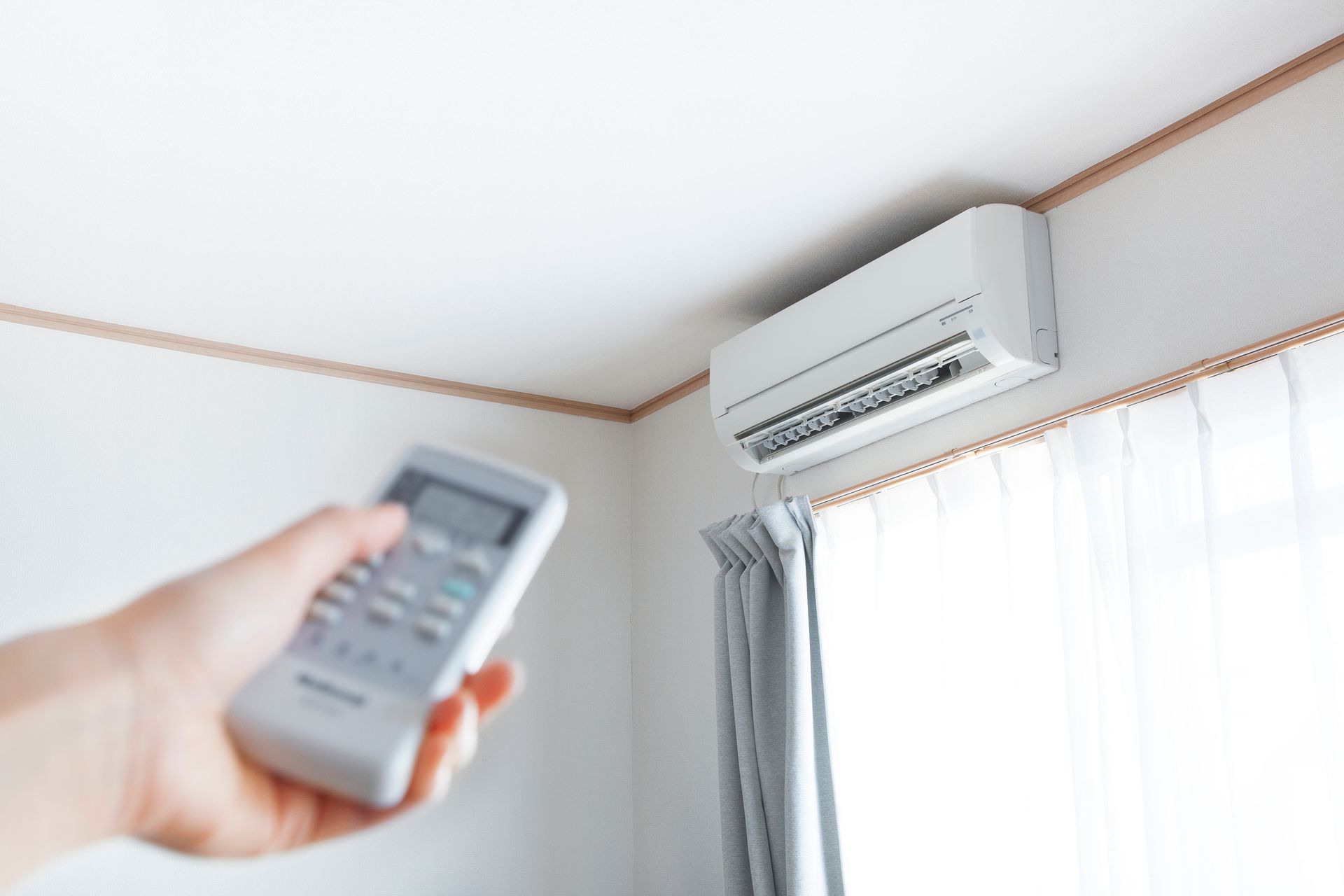 A hand with a remote control directed to the AC.