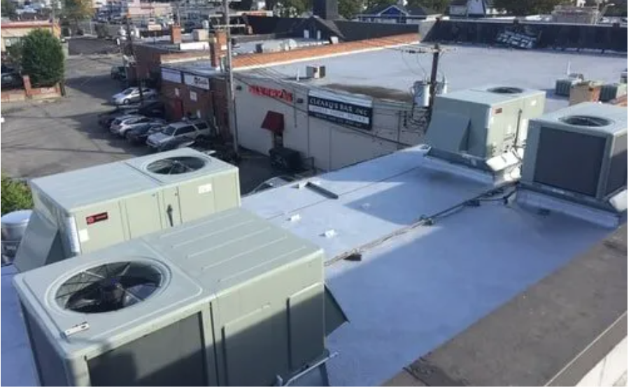 Rooftop view of commercial building, gray HVAC units, cars, and other buildings.