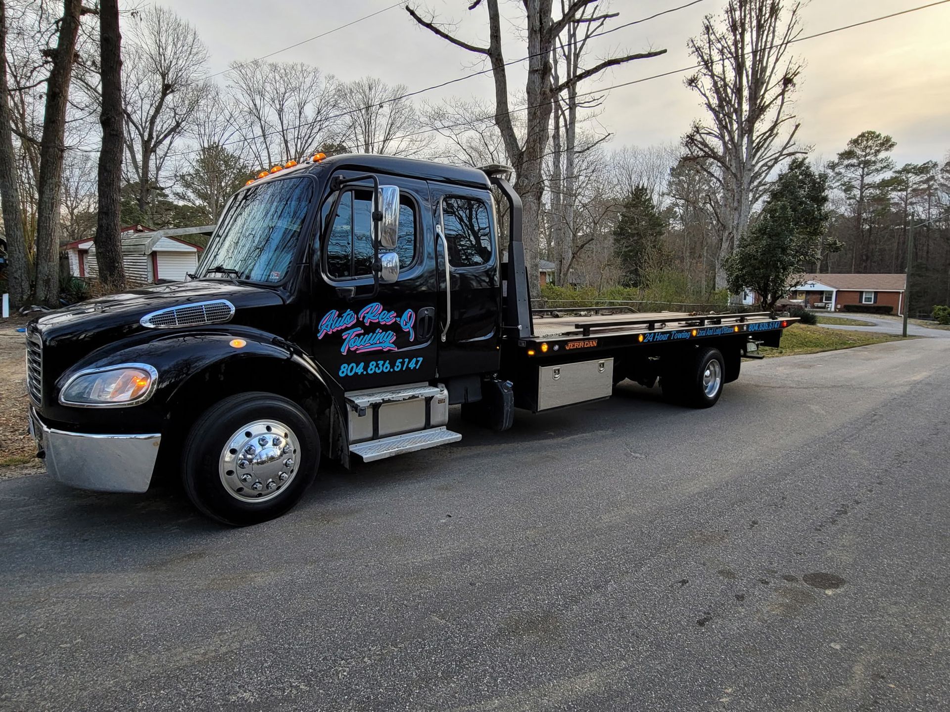 Black tow truck on a paved road; the truck is parked and has the company logo 