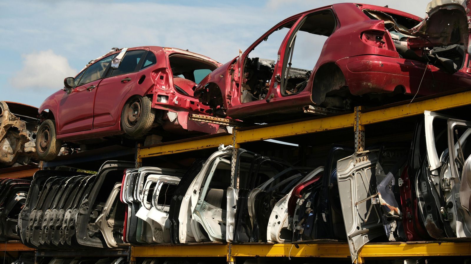 Red car frames stacked on top of car doors in a salvage yard.