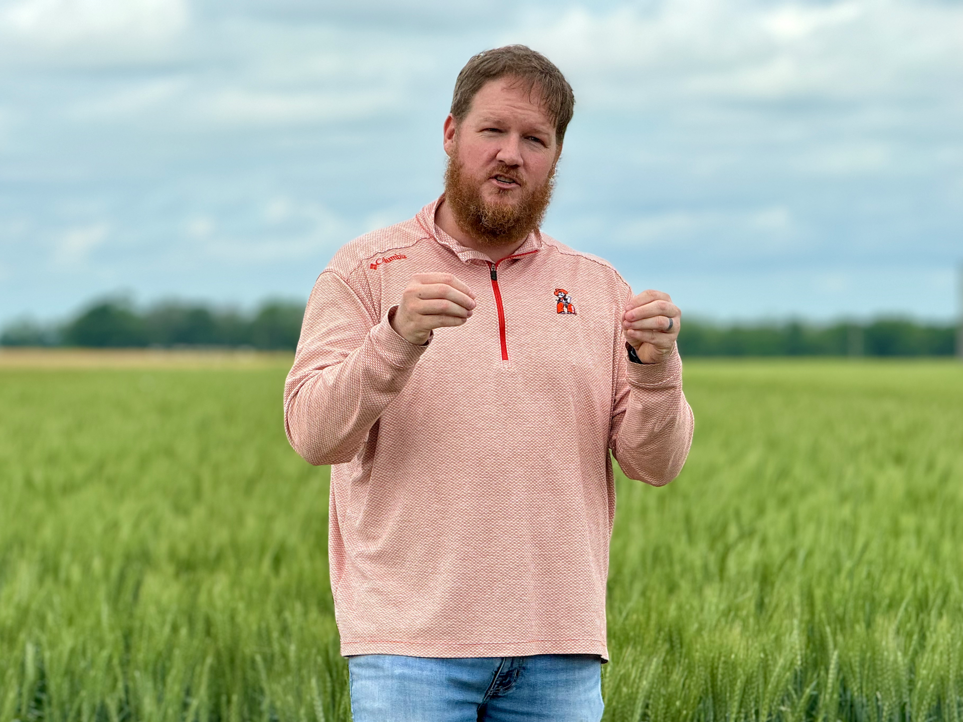 Man standing in a green field, holding up two objects against a cloudy sky.