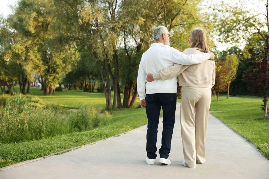 Two people walking arm-in-arm on a park path surrounded by trees and greenery