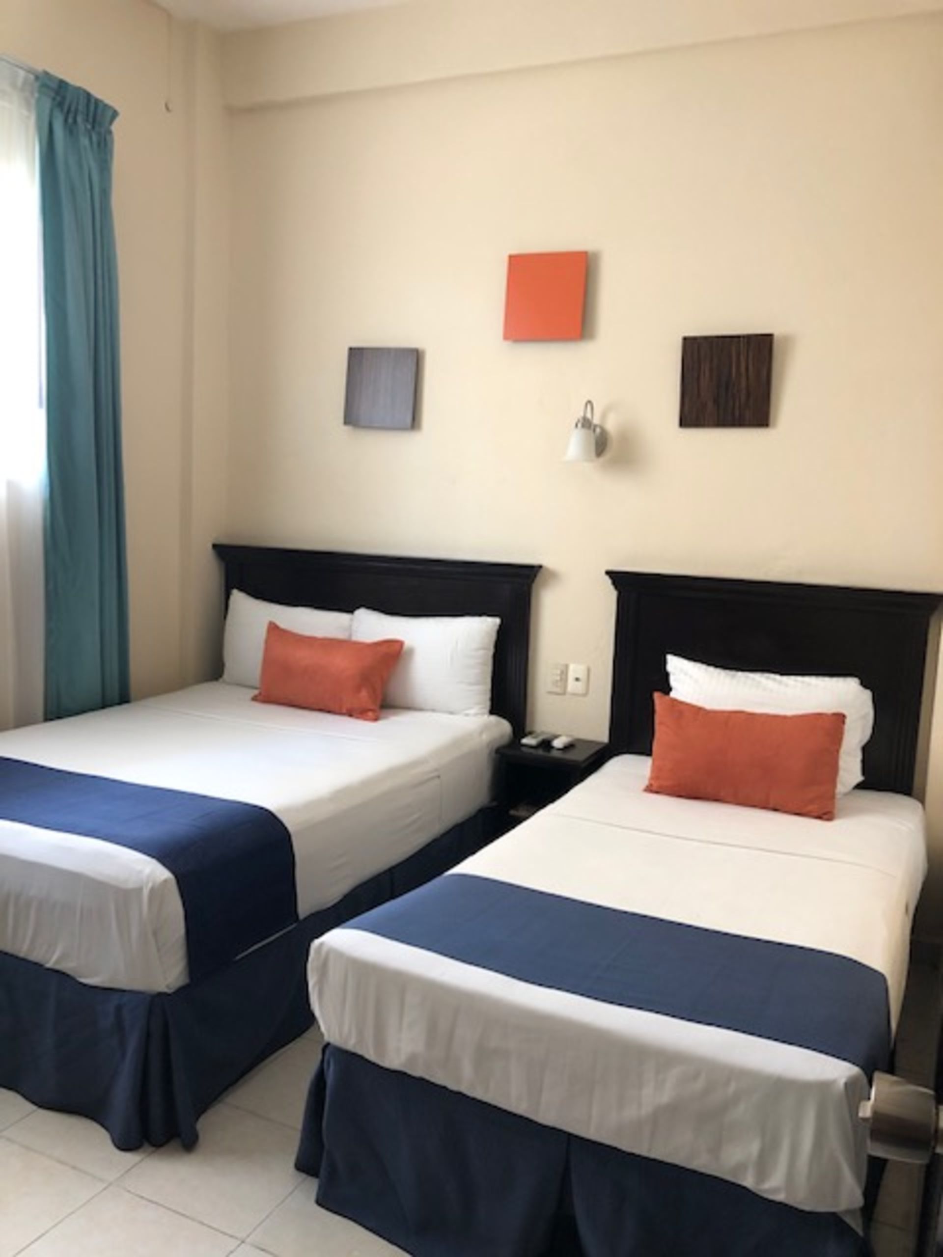 Dos camas en una habitación de hotel con ropa de cama blanca, detalles en azul marino y almohadas naranjas. 