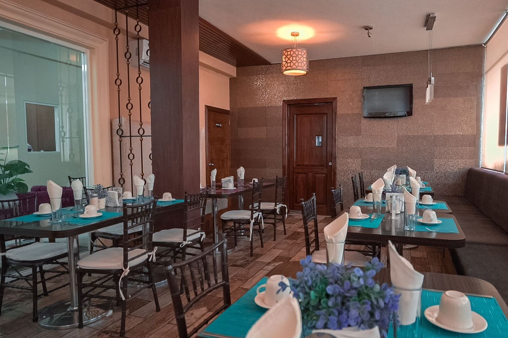 Comedor de restaurante con mesas preparadas para el servicio; manteles azules, sillas marrones, pared estampada.